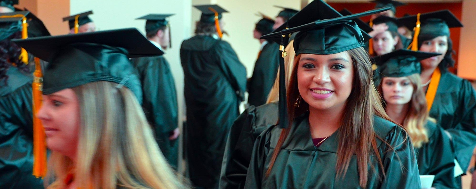 Graduates queuing in lobby with a girl highlighted showing excitement about graduating.