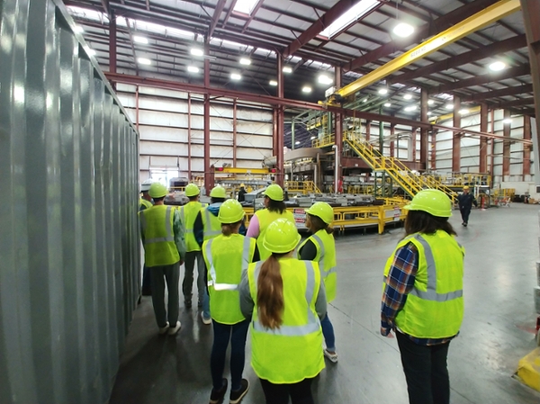 Bridge students visit a manufacturing plant, seen here  wearing hi-vis vest and helmet.