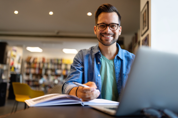 Man writing in notebook, smiling at camera