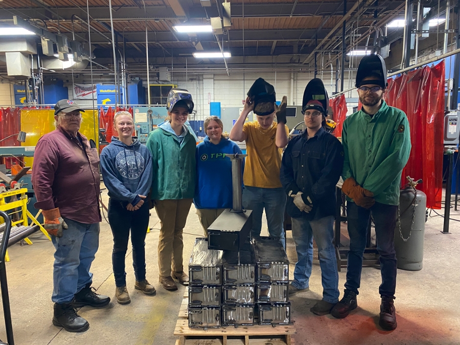 A group of young men and women who are students in the welding program at Isothermal Community College. They are posing with the stoves they made to help hurricane victims in Western North Carolina.